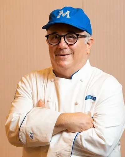 Chef Mark Strausman in his whites and a blue M cap, arms folded
