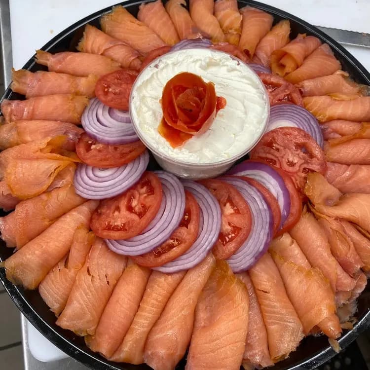 A catering platter of smoked salmon rosettes, sliced tomato and red onion around whipped cream cheese