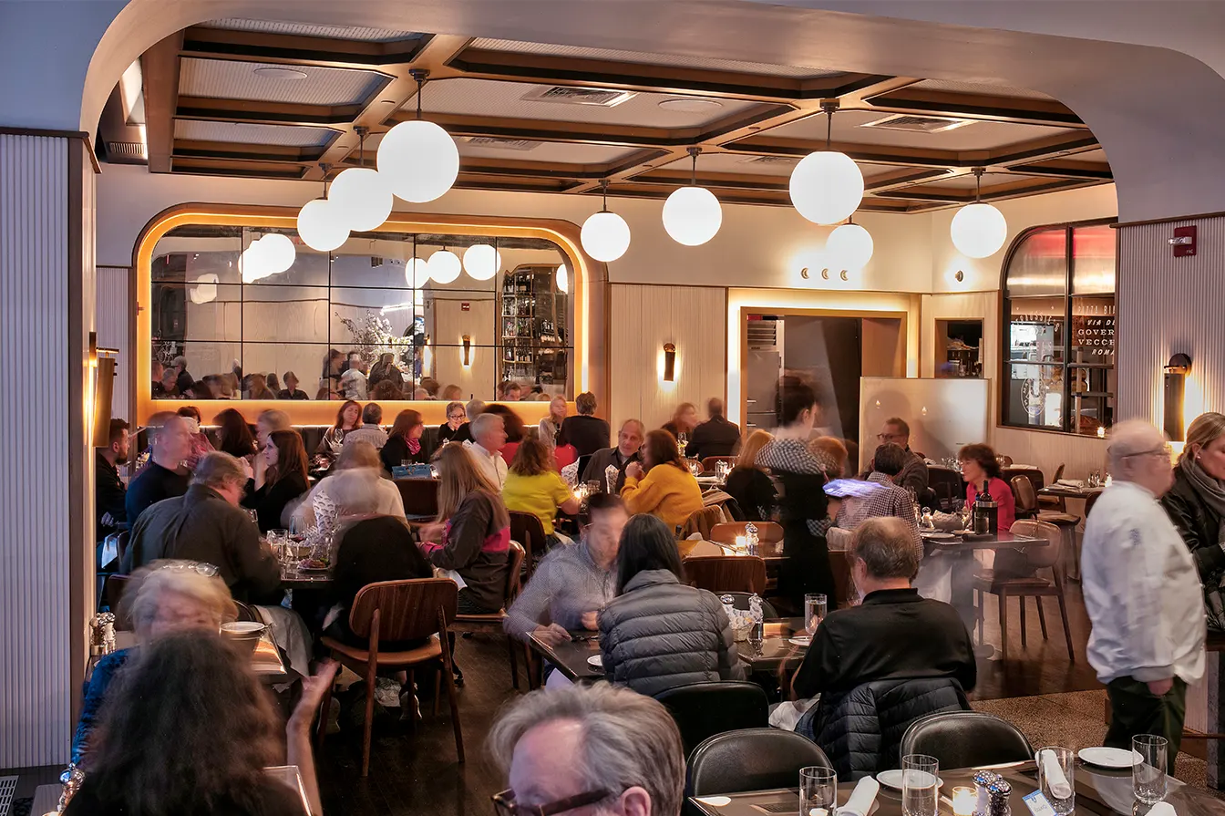The dining room on a busy evening, under globe pendant lights and a coffered ceiling