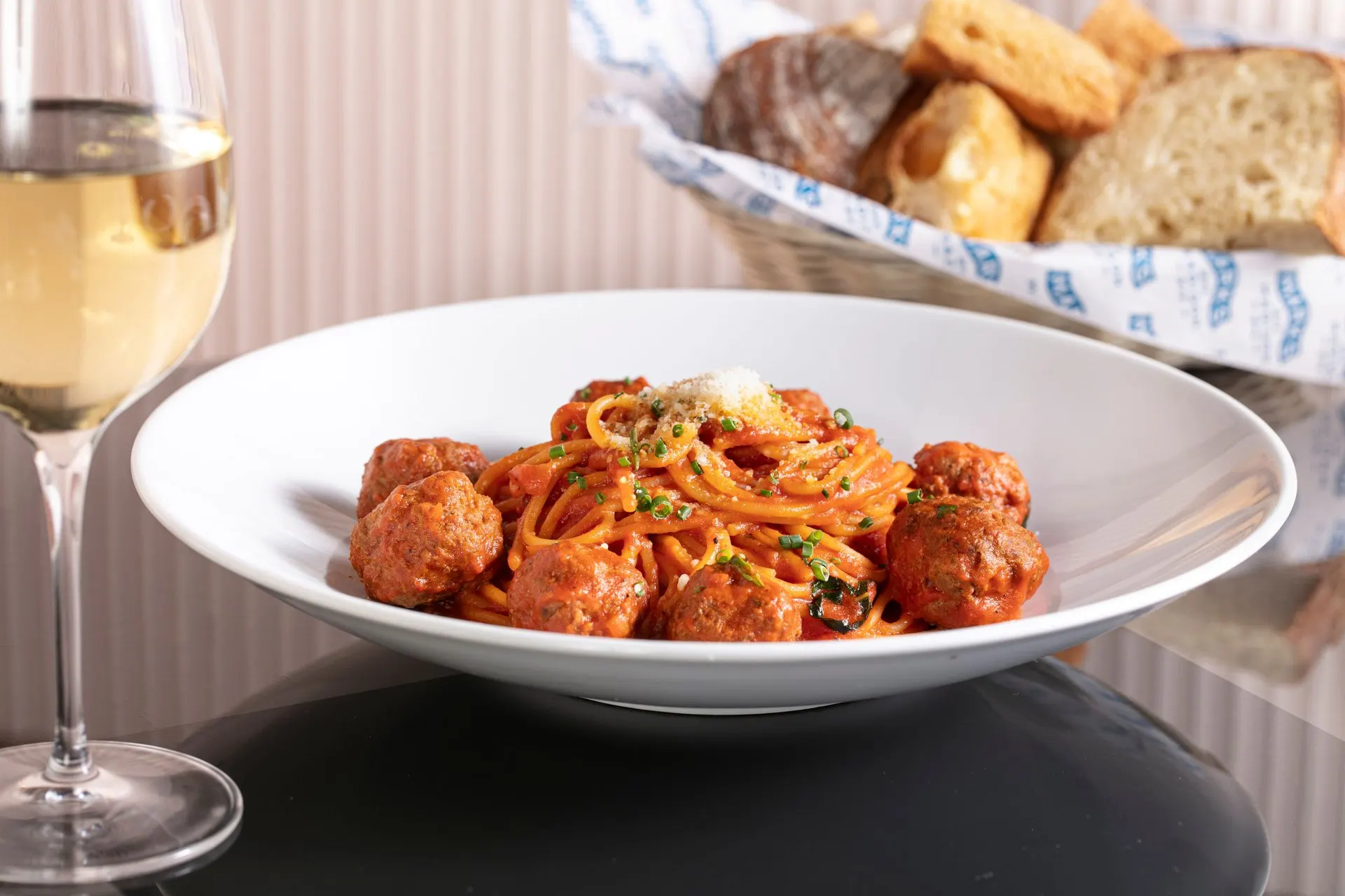 Spaghetti and meatballs with a glass of white wine and a basket of house-baked bread