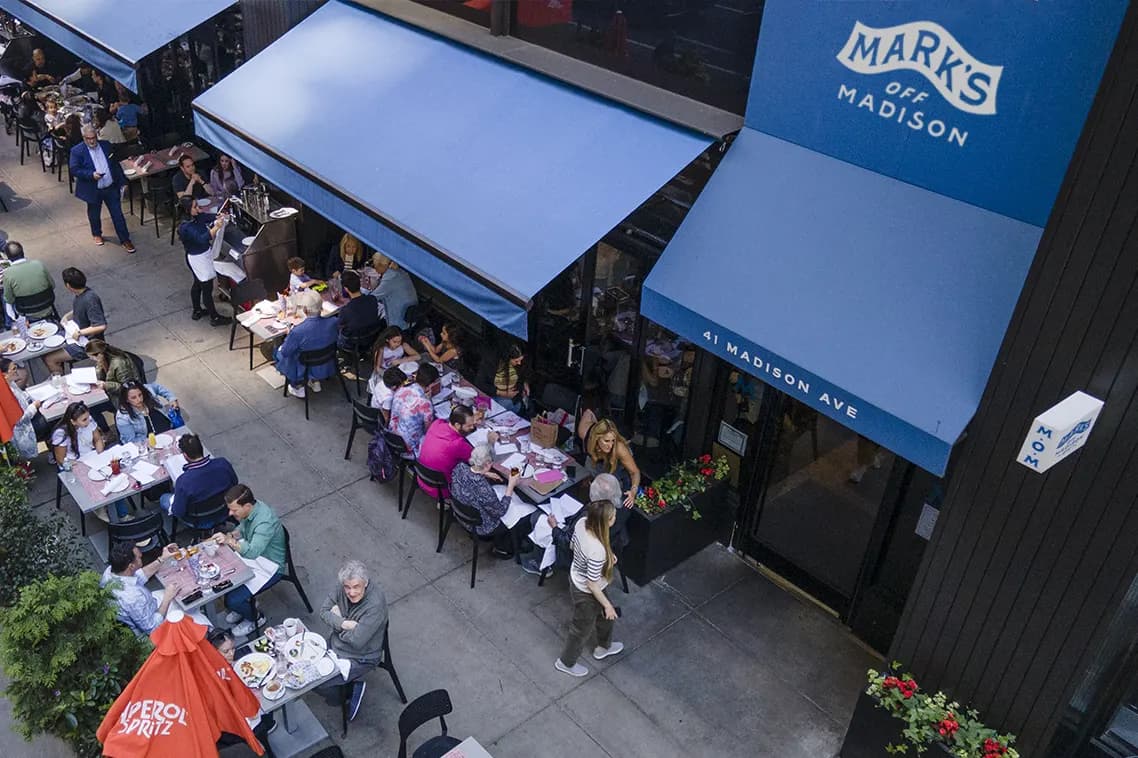 Looking down on the sidewalk tables under the blue Mark’s Off Madison awnings